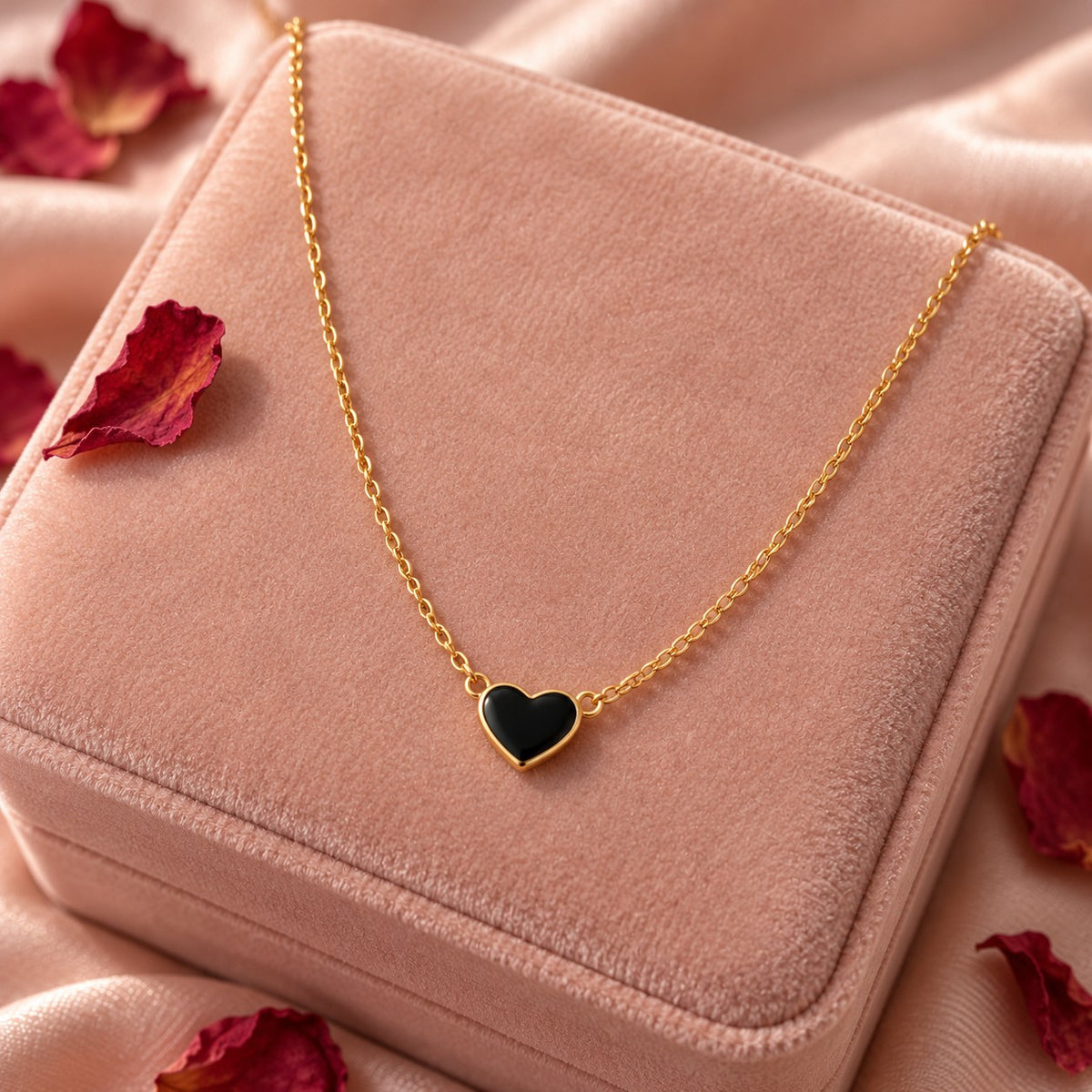 Gold black heart pendant chain necklace on a blush-pink velvet jewellery box