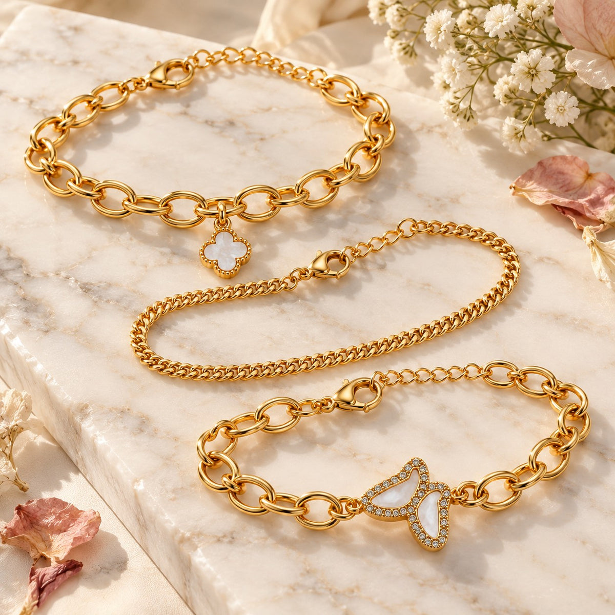 Gold clover and butterfly bracelets styled on white marble with soft flowers