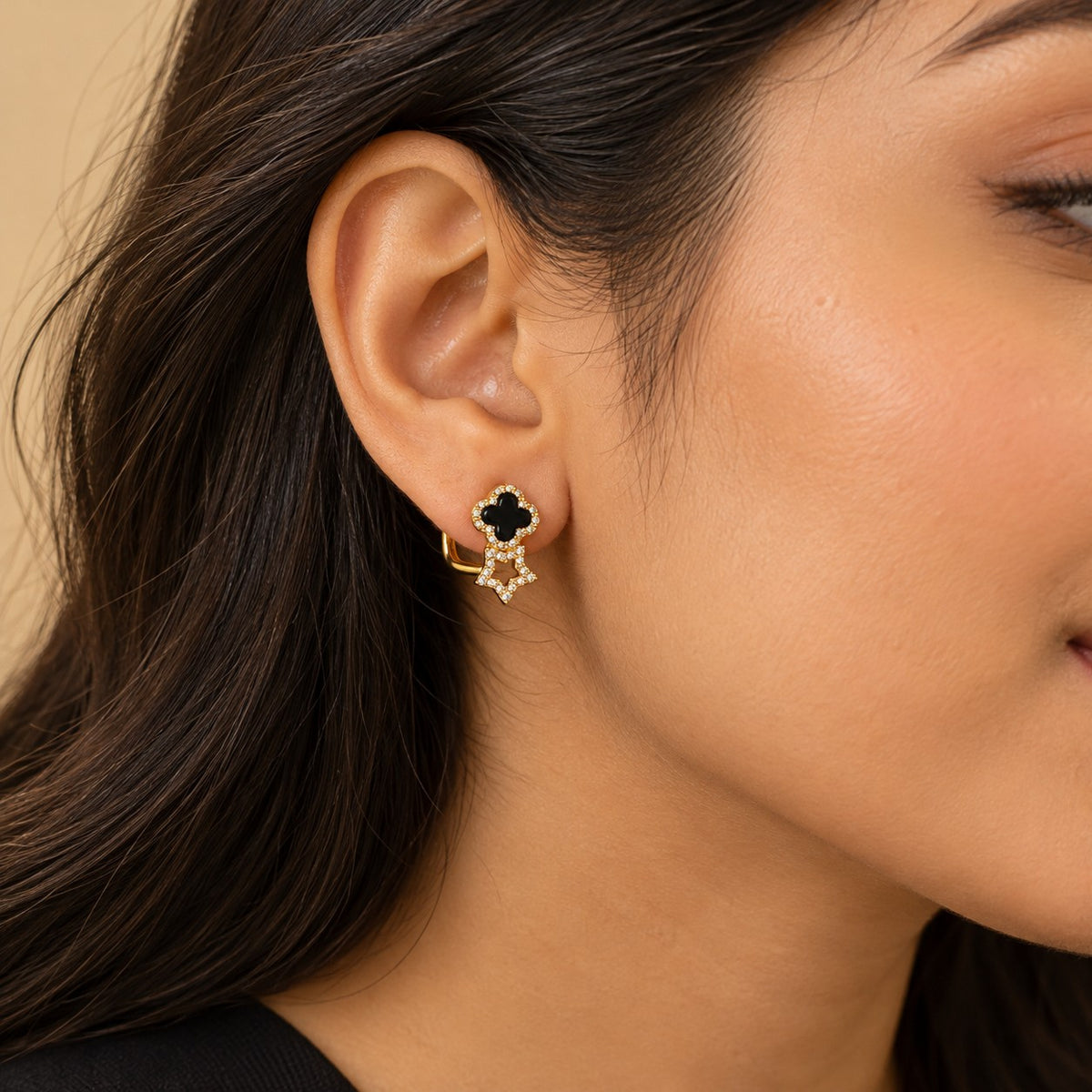 Woman wearing a gold clover and star huggie hoop earring, close-up of ear and jawline