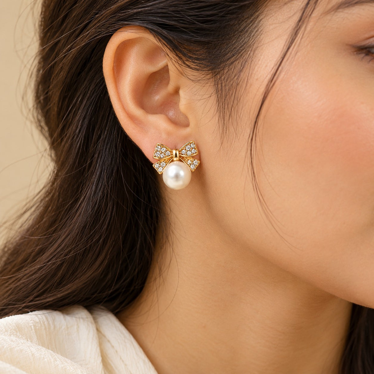 Woman wearing gold crystal bow pearl stud earrings, close-up of earlobe and jawline