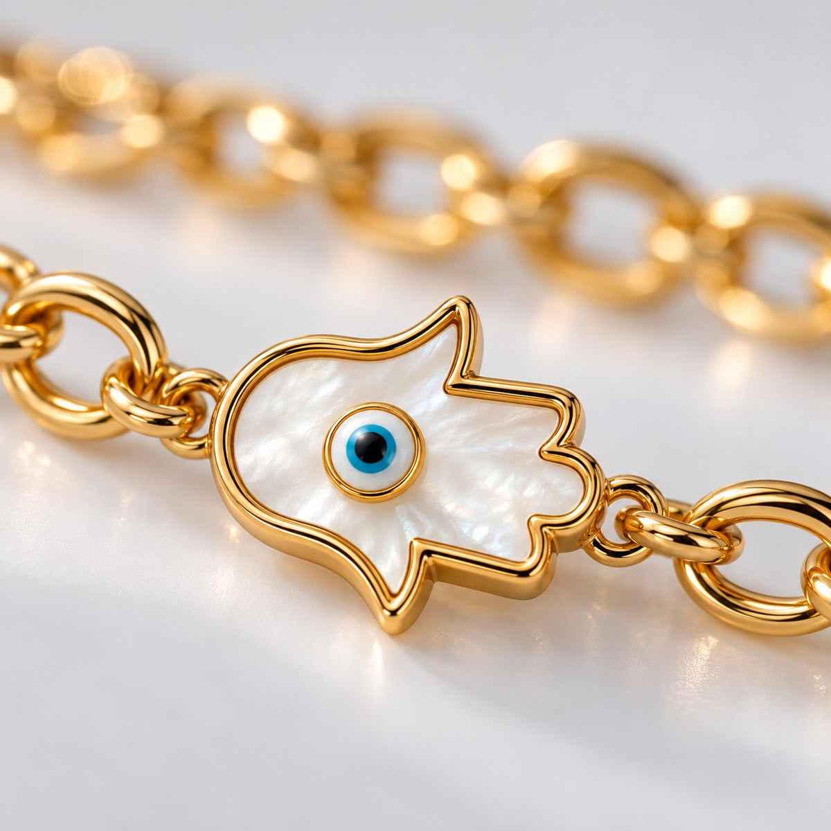 Close-up of the white enamel hamsa hand with a blue evil eye on the gold bracelet