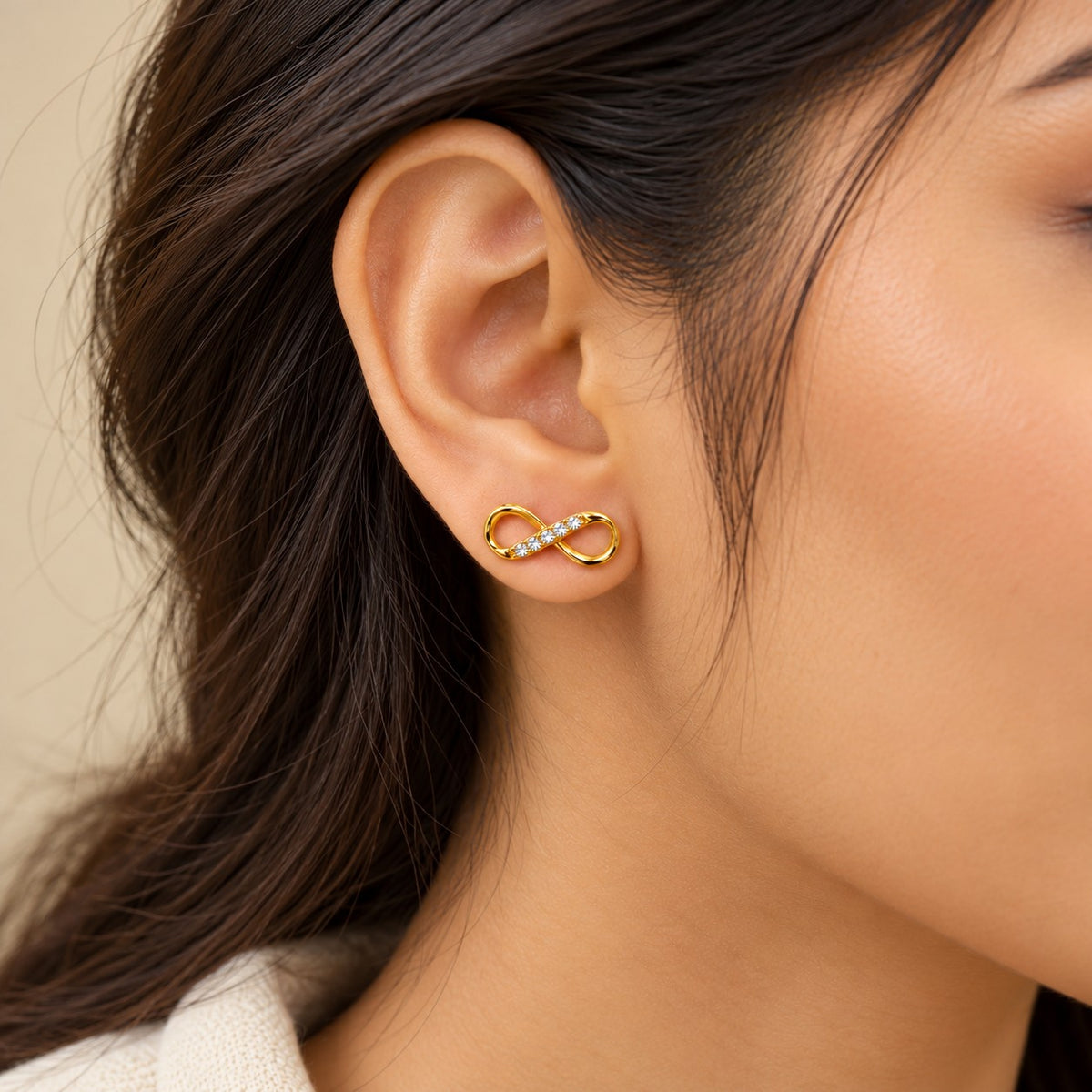 Woman wearing gold infinity crystal stud earrings, close-up of earlobe and jawline