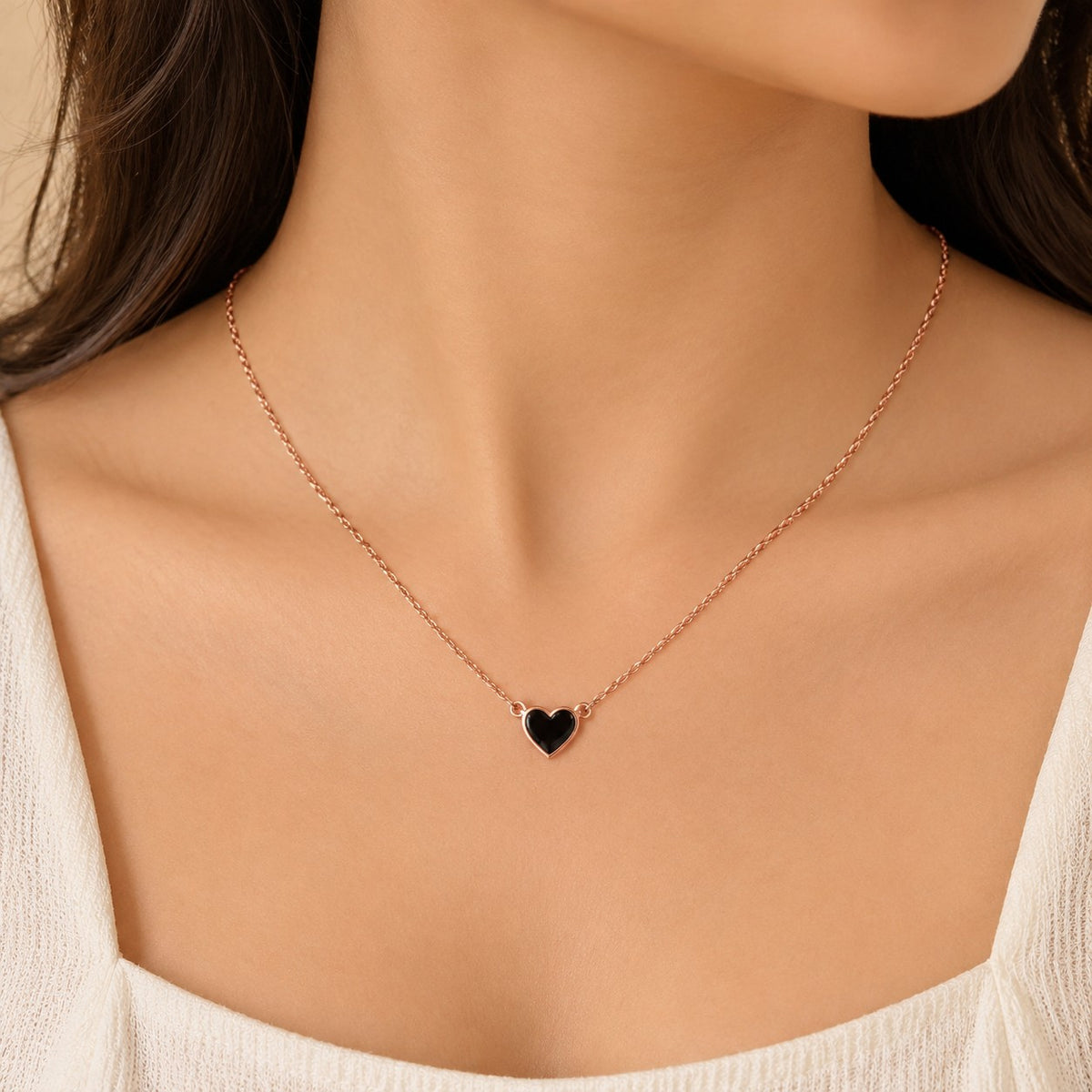 Woman wearing a rose gold chain necklace with a small black heart pendant