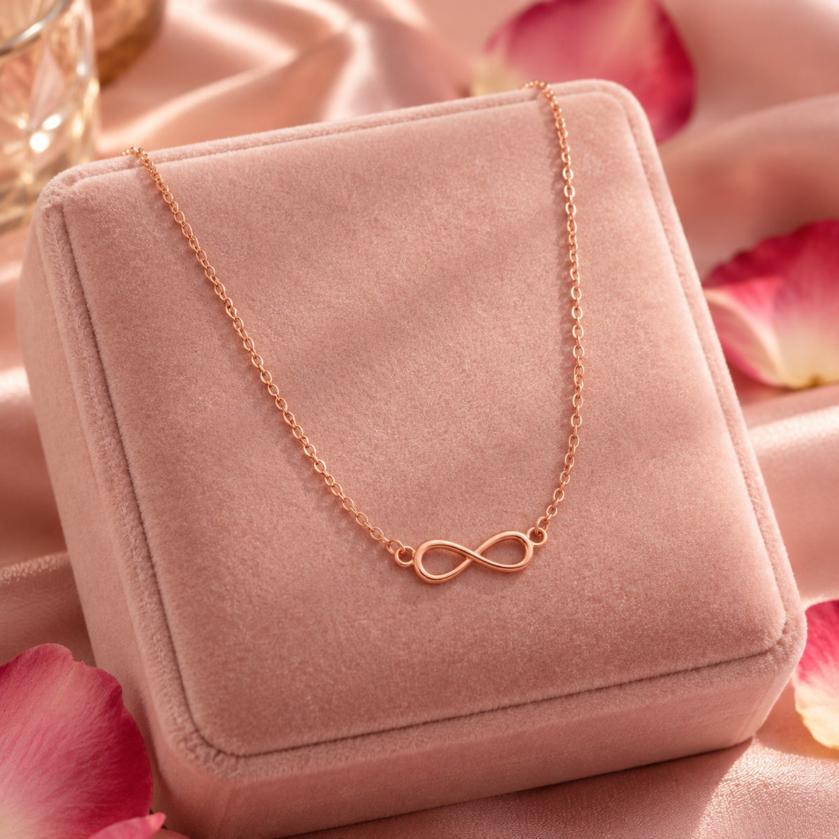 Rose gold infinity pendant chain necklace on a blush velvet jewellery box with rose petals