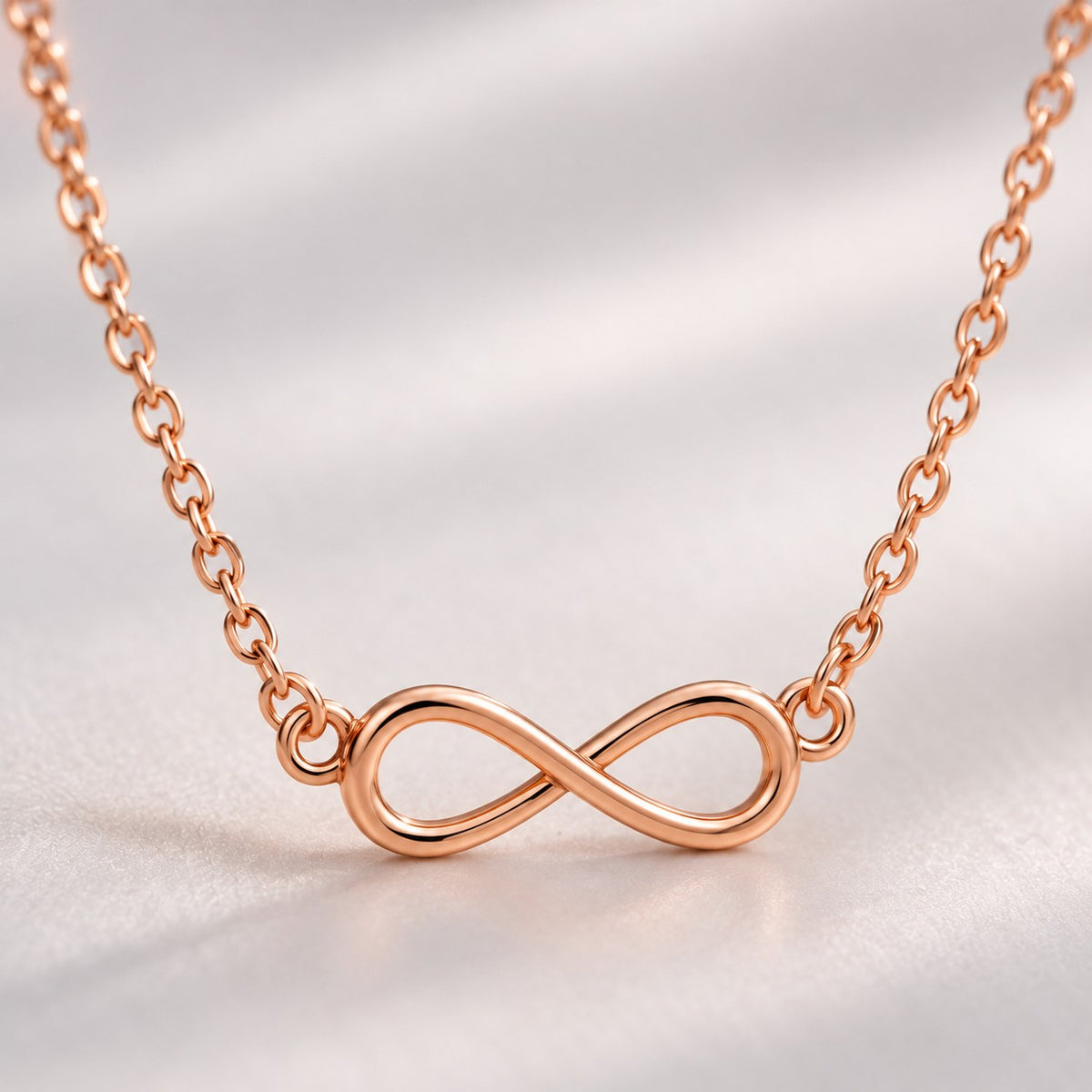 Macro view of the open rose gold infinity pendant and fine chain links