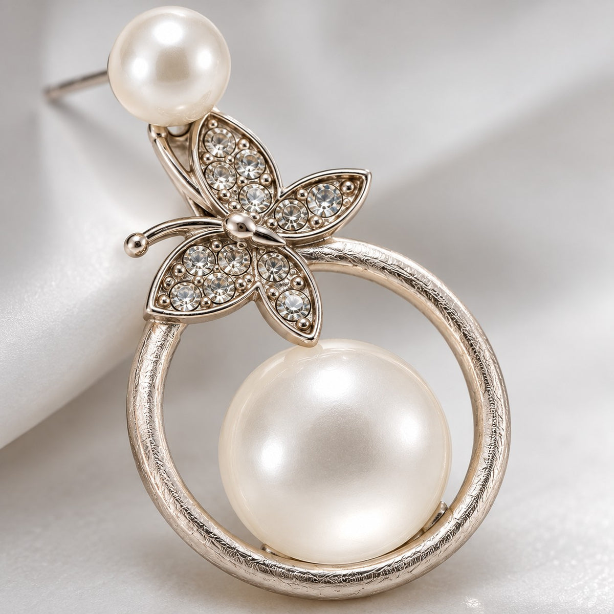 Macro view of the crystal butterfly and milky faux pearl on a silver circle drop earring