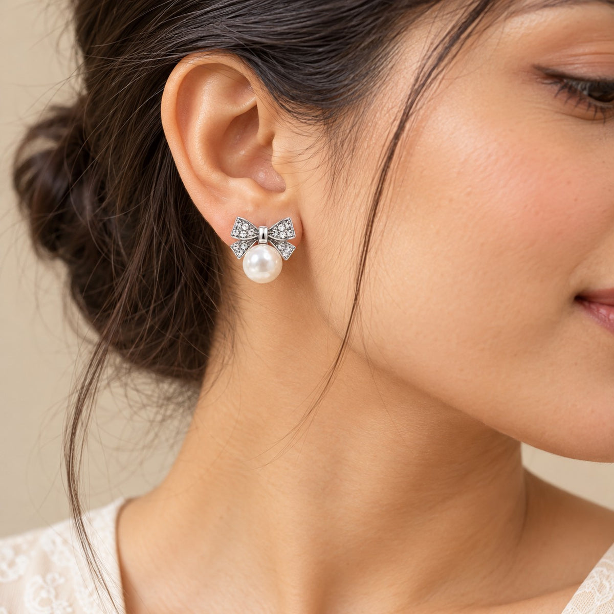 Woman wearing silver crystal bow pearl stud earrings, close-up of earlobe and jawline