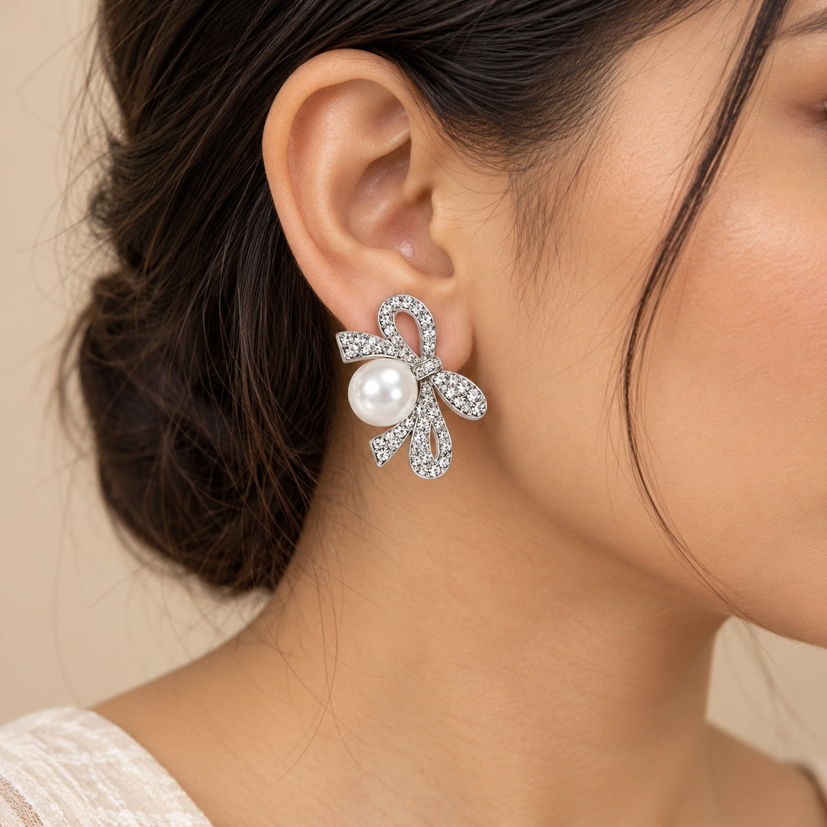Woman wearing silver crystal ribbon bow pearl drop earrings, close-up of ear and jawline