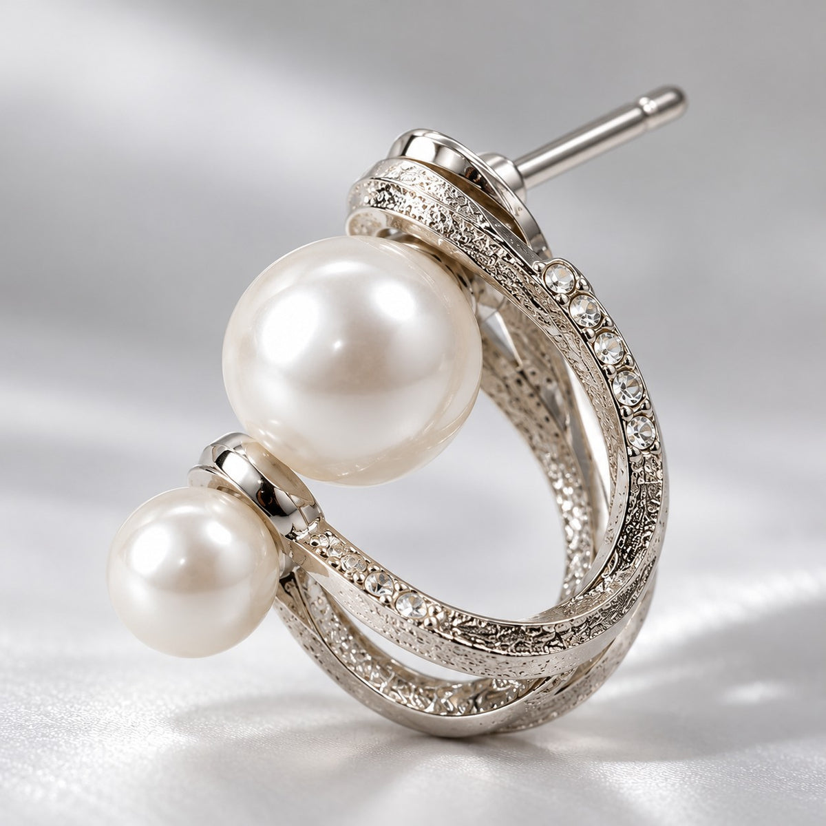 Close-up of the twisted silver bands and faux pearls on a double pearl hoop stud earring
