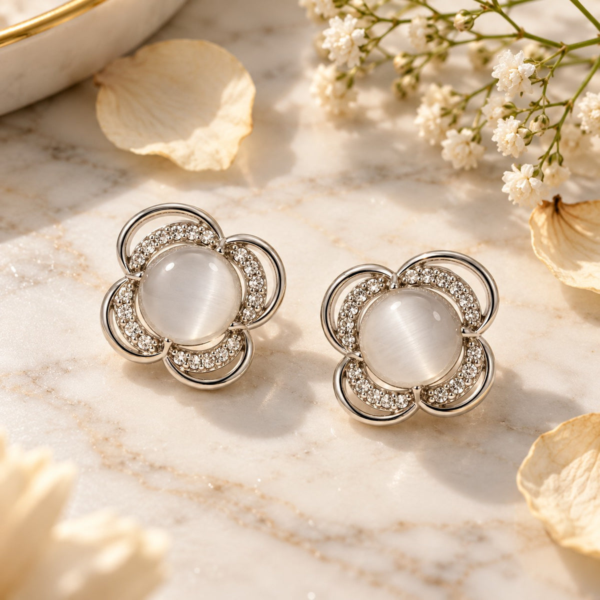 Silver flower cat eye stone stud earrings on white marble with soft dried petals