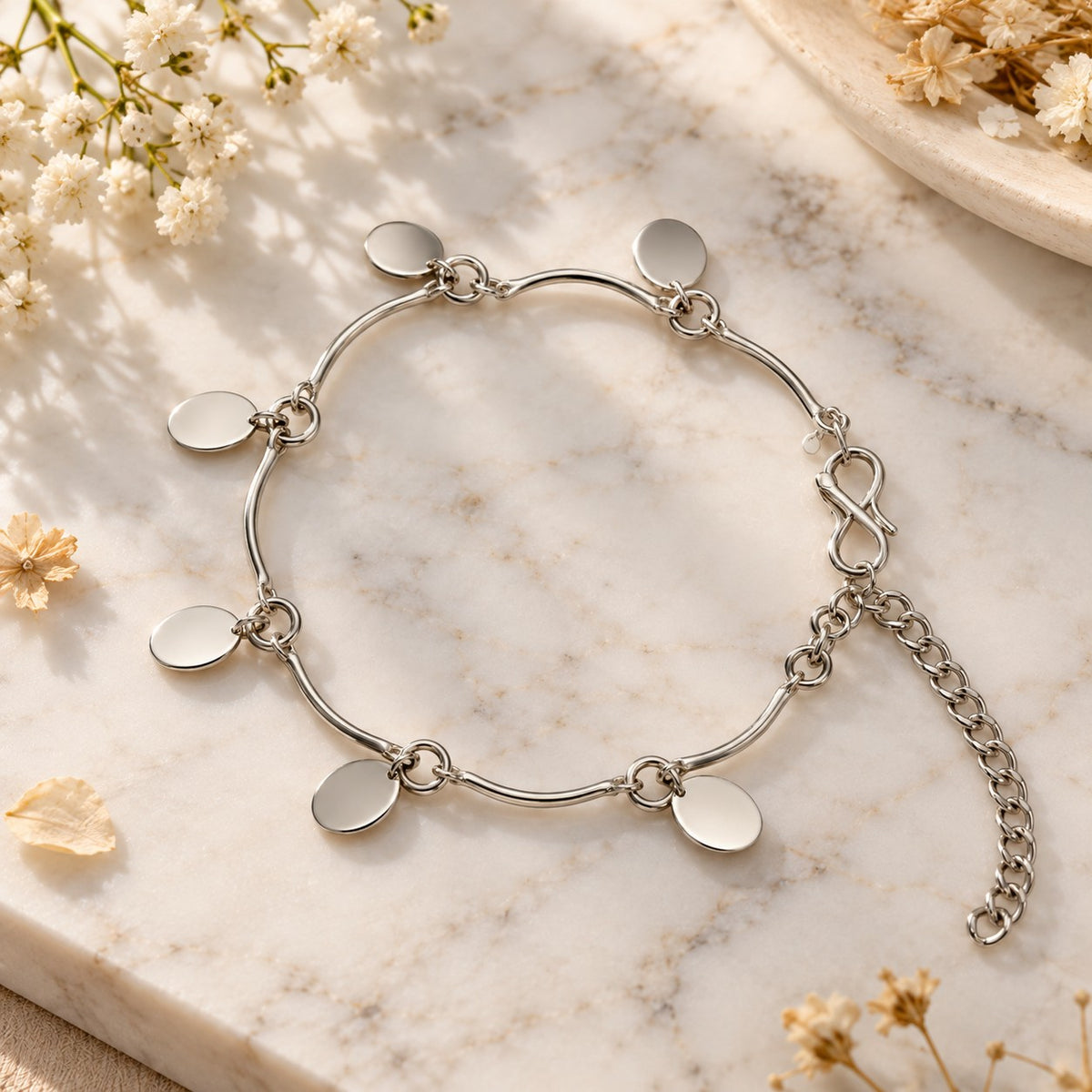 Silver oval disc charm bracelet styled on white marble with soft flowers