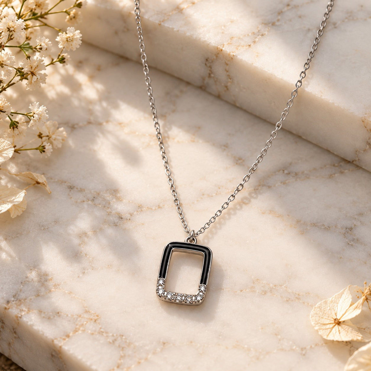 Silver rectangle pendant chain necklace styled on white marble with soft flowers