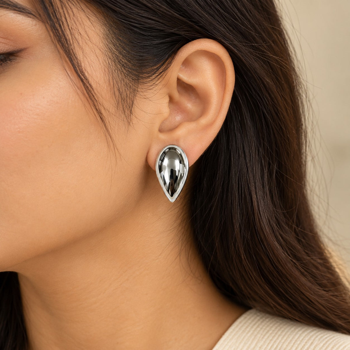 Woman wearing silver teardrop dome stud earrings, close-up of earlobe and jawline
