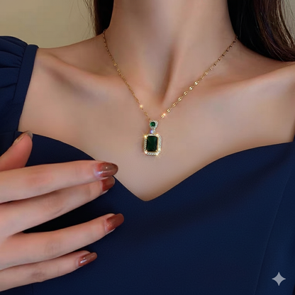 Gold necklace with a green gemstone pendant worn by a person in a navy blue dress.
