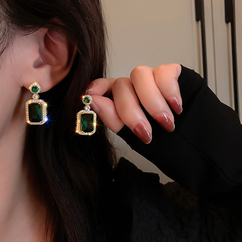 Person wearing green gemstone earrings with gold accents