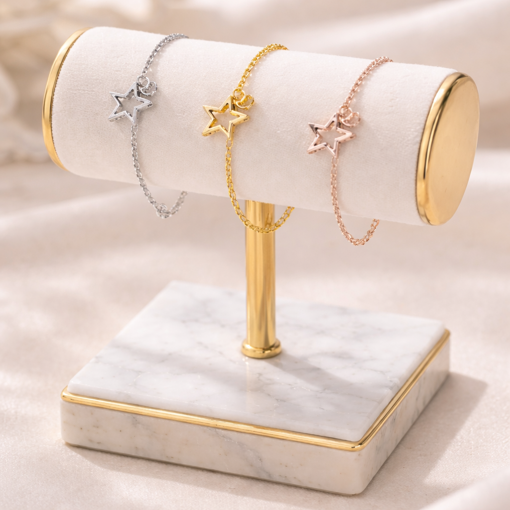 Silver, gold, and rose gold star charm bracelets for women, elegantly displayed on a white velvet stand with a marble base.