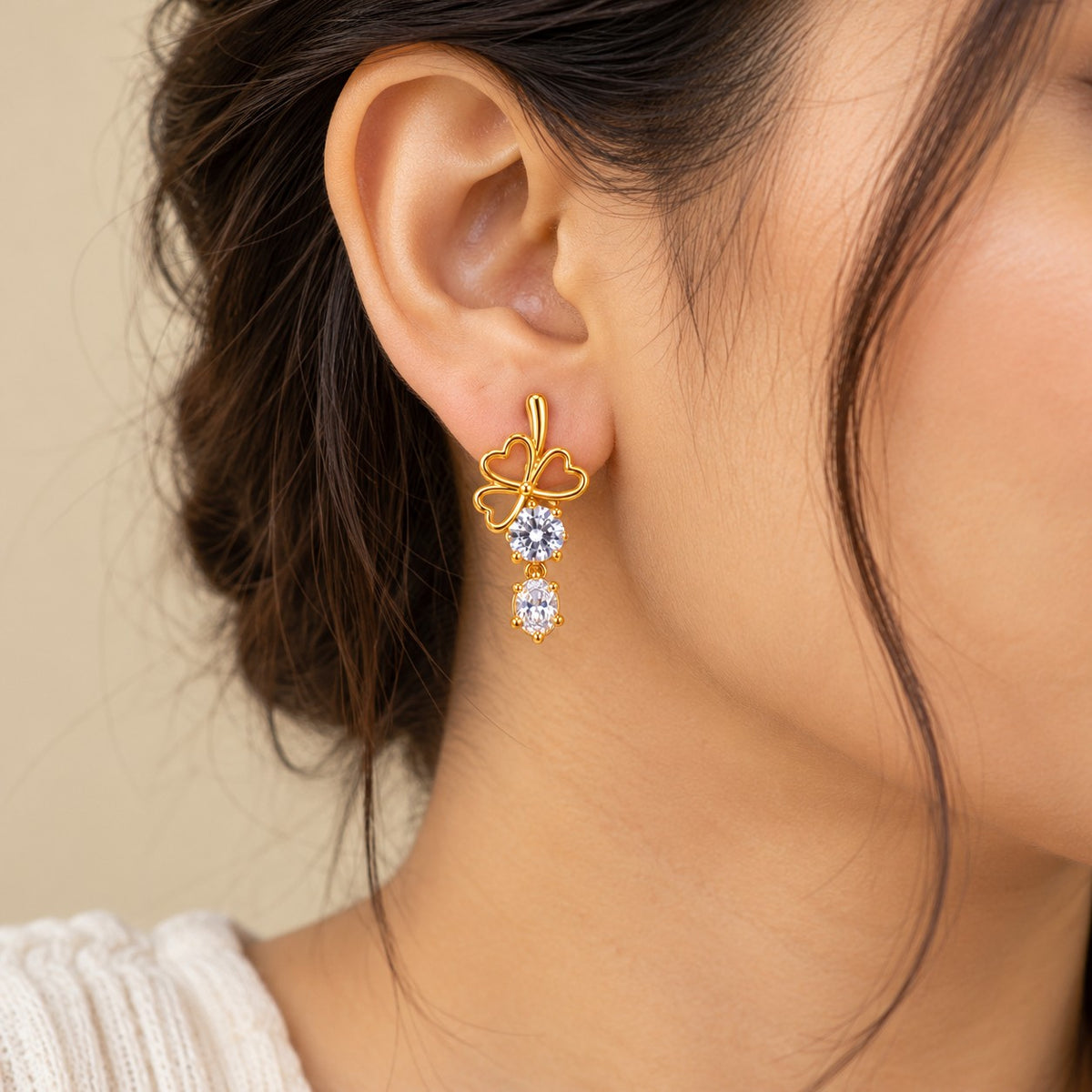 Woman wearing gold AD stone drop earrings with clover design, close-up of ear and jawline