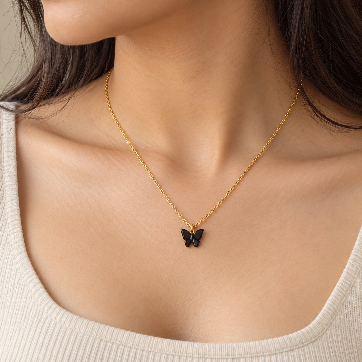Woman wearing a gold chain necklace with a small black butterfly pendant