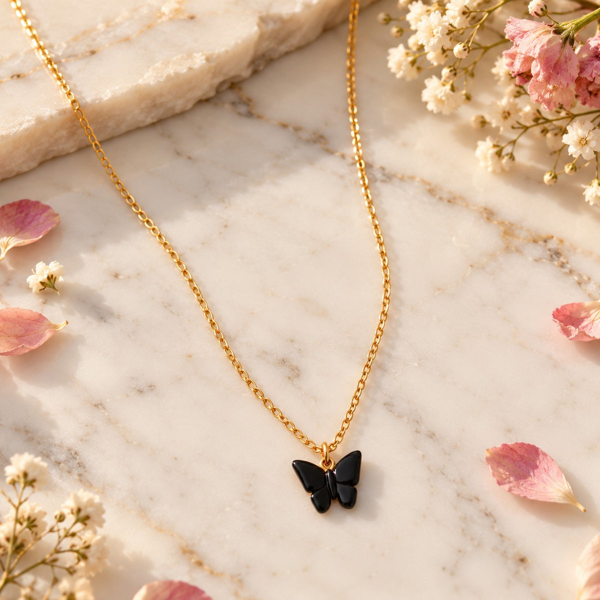 Gold black butterfly pendant necklace styled on white marble with soft flowers