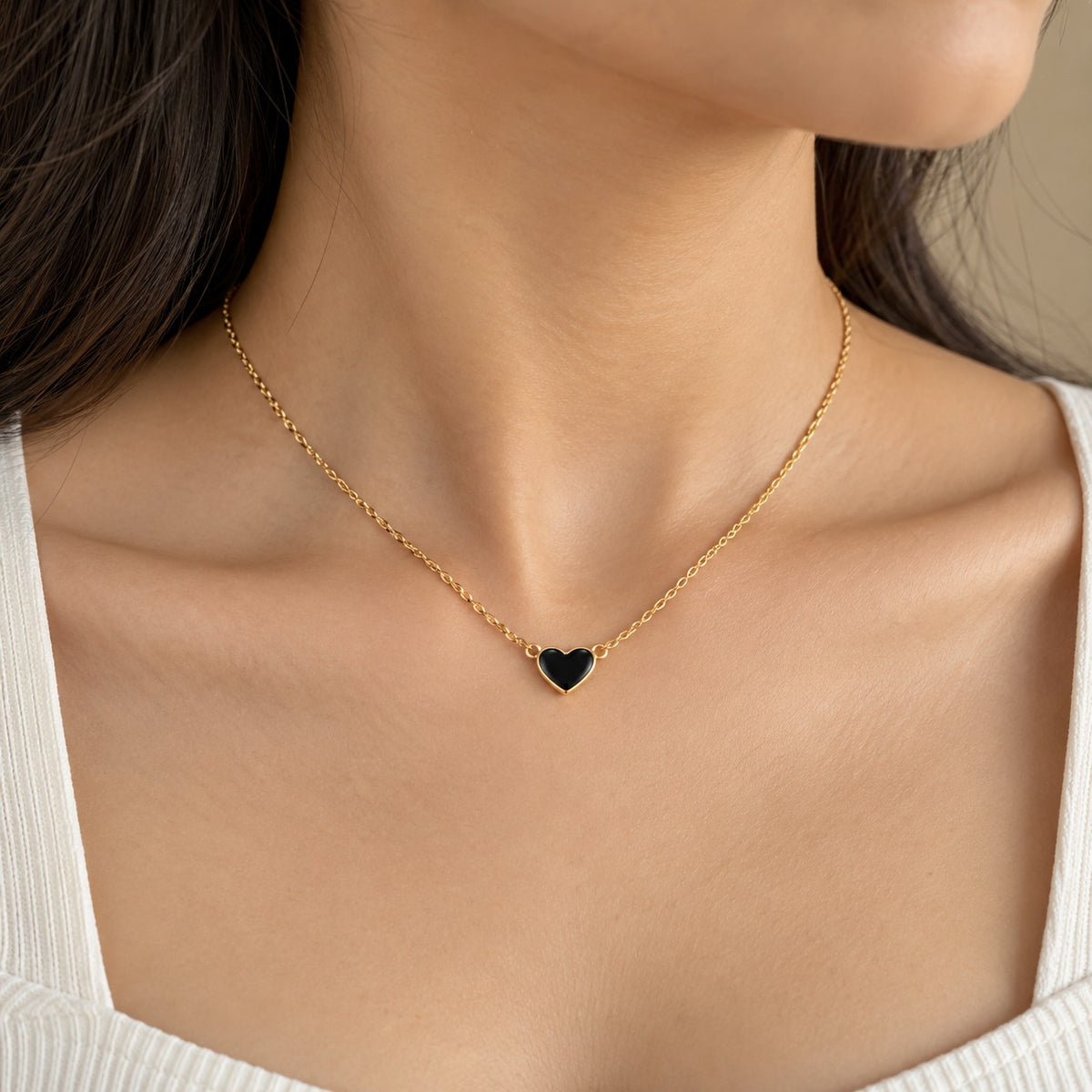Woman wearing a gold chain necklace with a small black heart pendant