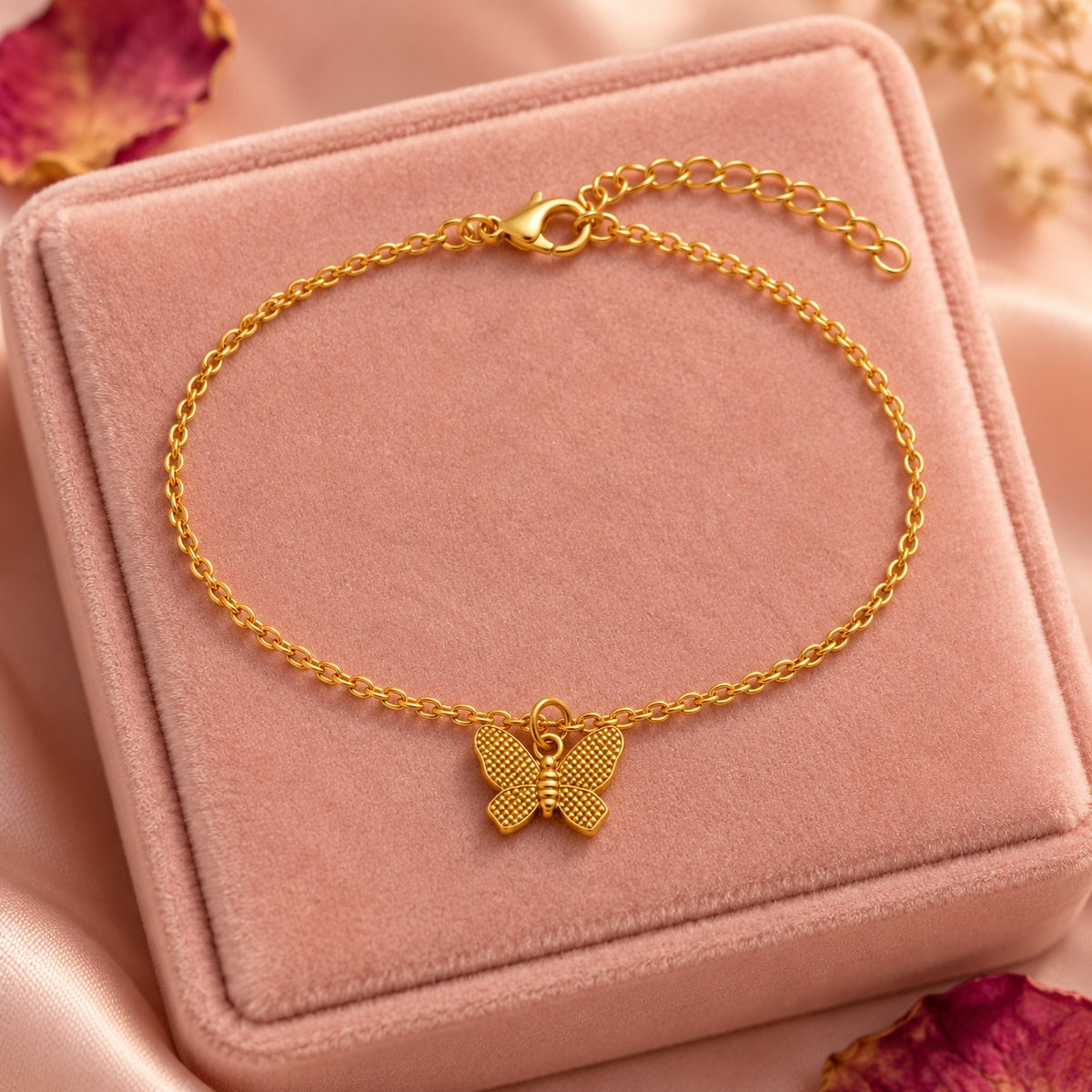Gold butterfly charm bracelet styled on a blush velvet box with dried petals