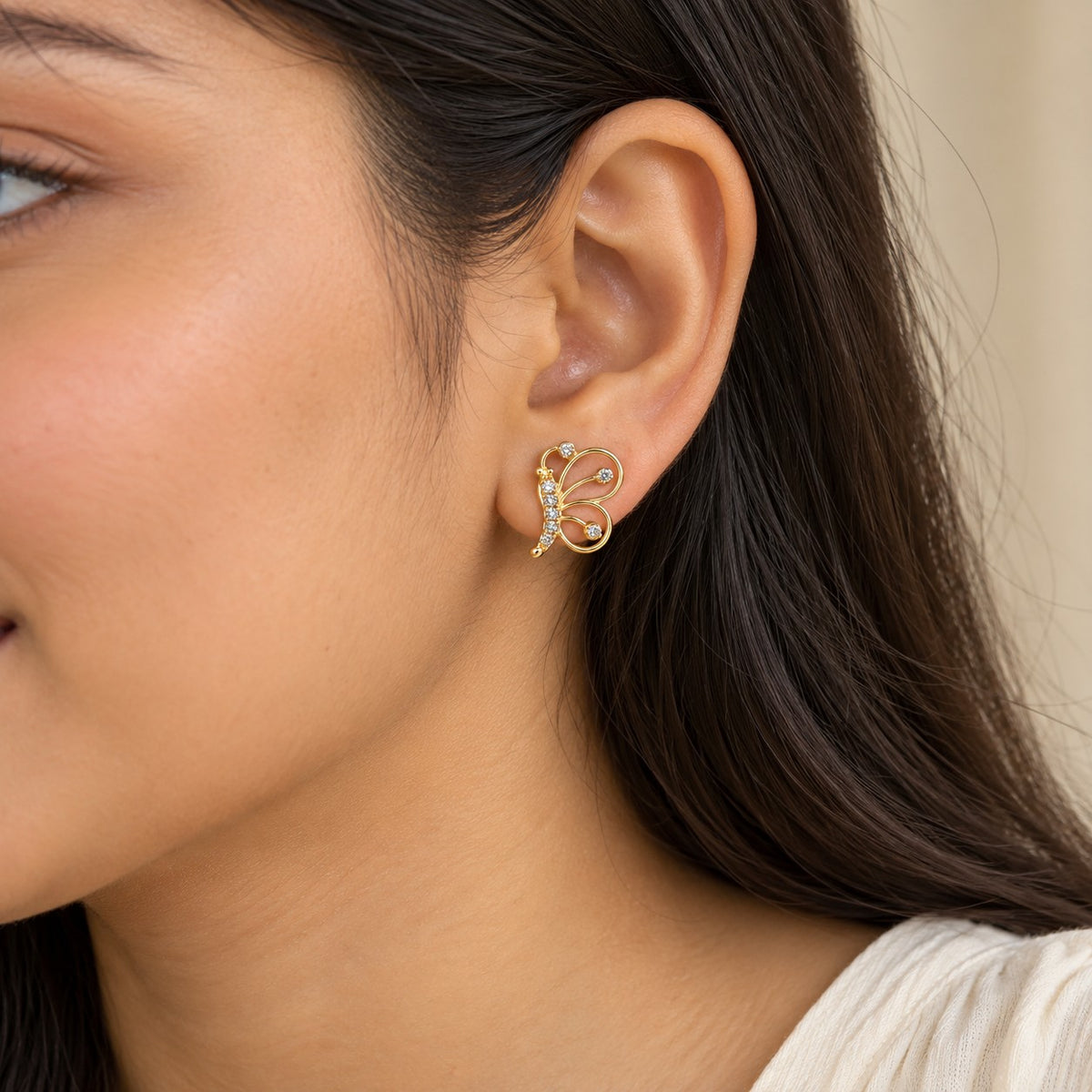 Woman wearing a gold butterfly stud earring with crystals, close-up of ear and jawline