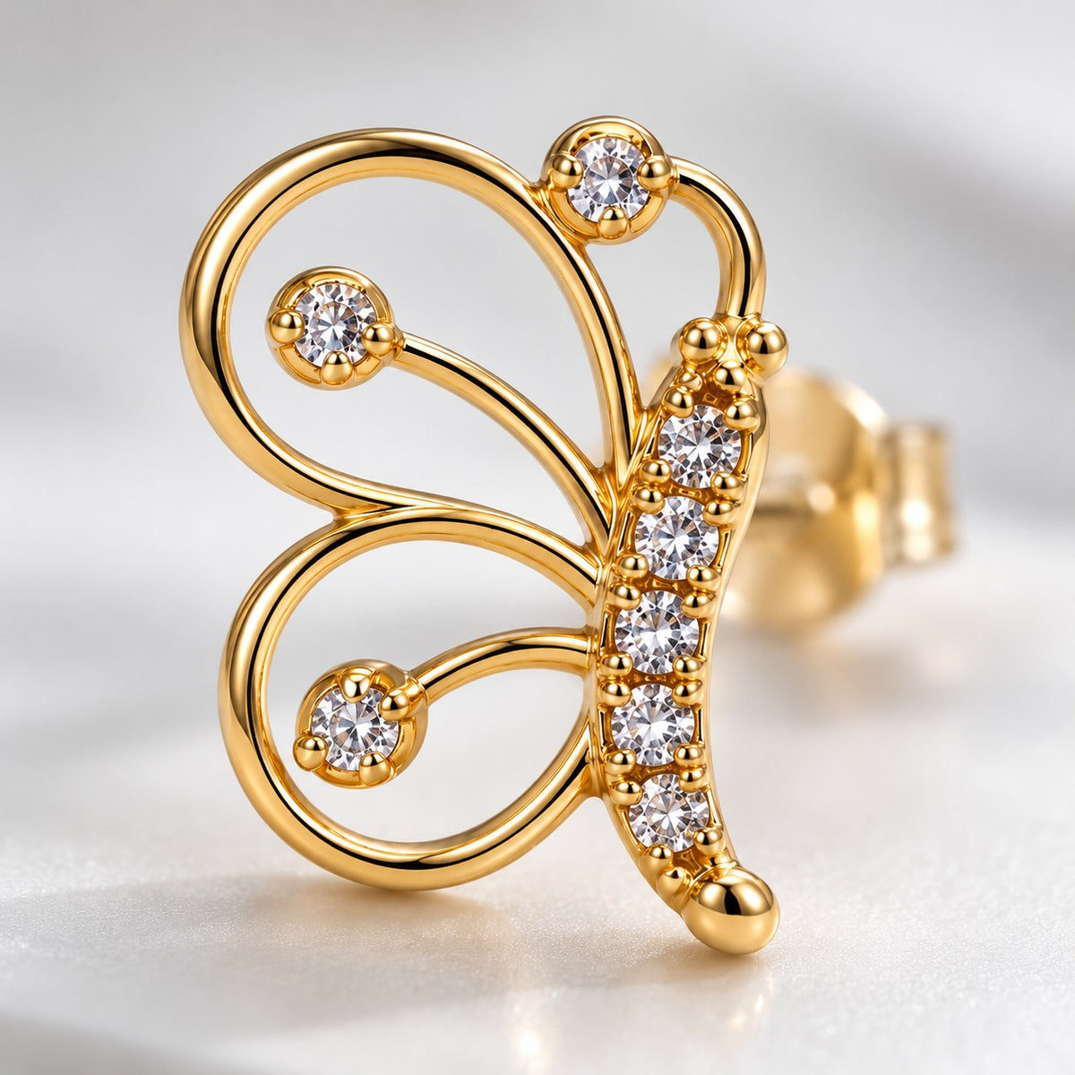 Close-up of the open-wire wings and crystal body of a gold butterfly stud earring