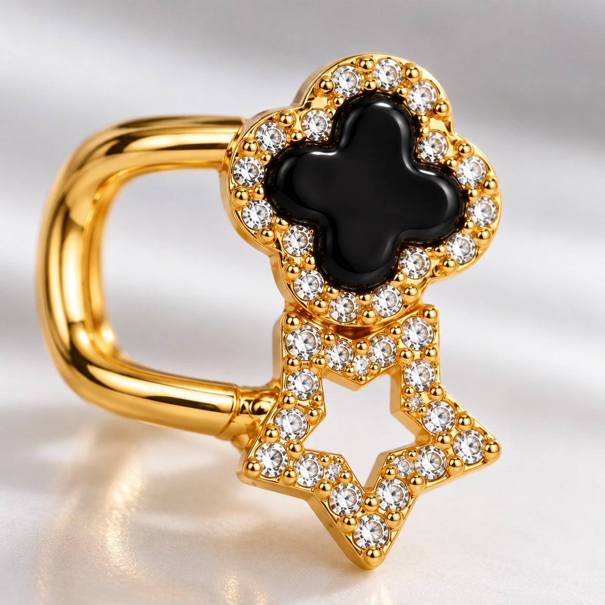 Close-up of crystal-edged black clover and open star on a gold huggie earring