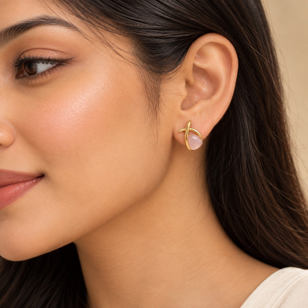 Woman wearing a gold crossover pink stone stud earring, close-up of ear and jawline