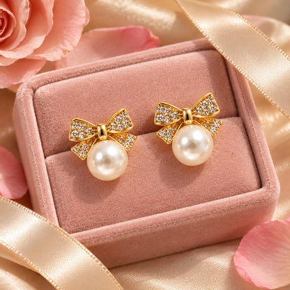 Gold crystal bow pearl stud earrings on a blush-pink velvet jewellery box with petals