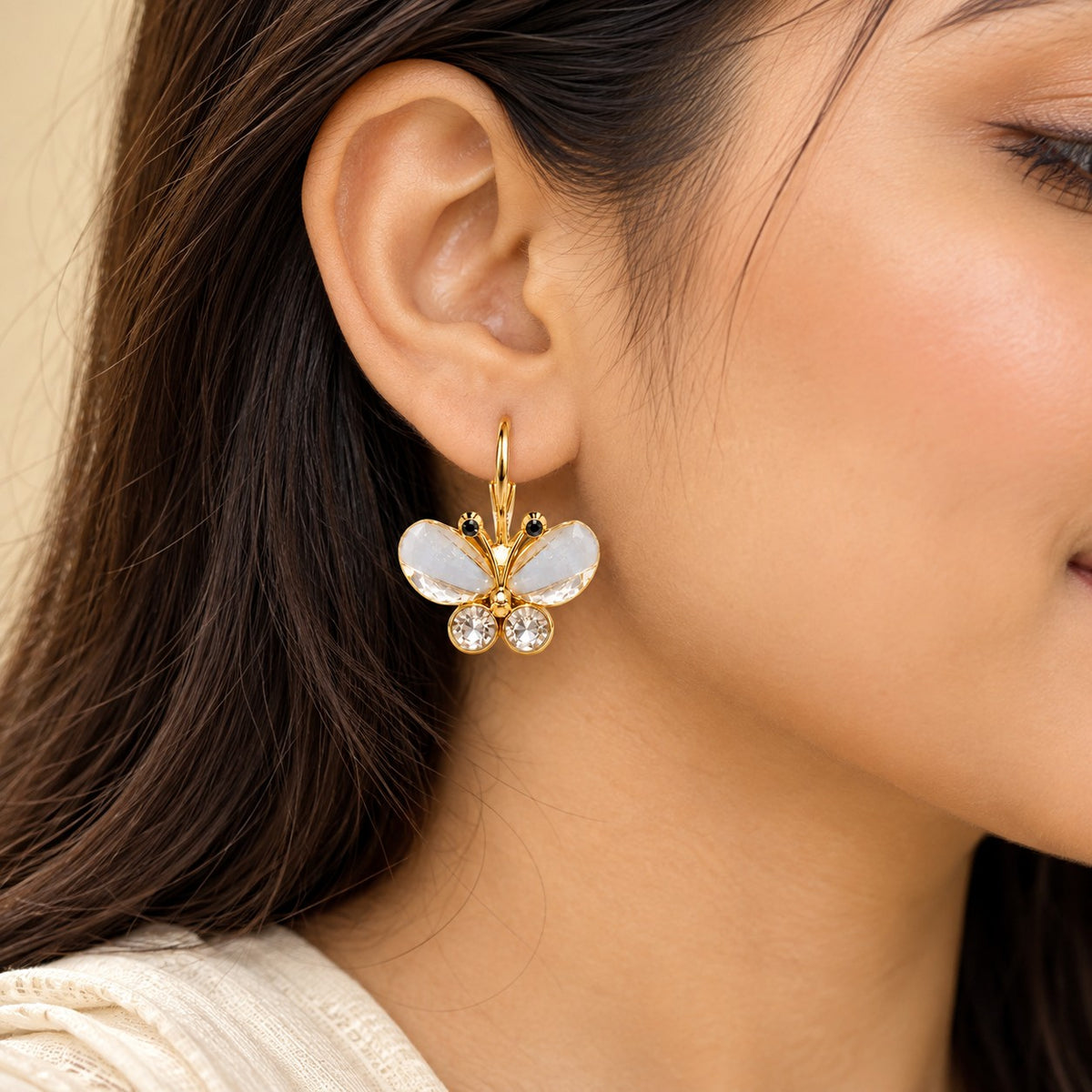 Woman wearing a gold crystal butterfly drop earring, close-up of ear and jawline