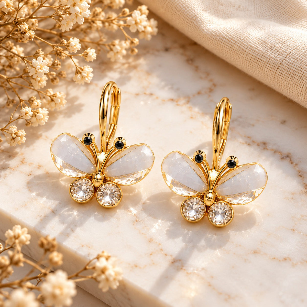 Gold crystal butterfly drop earrings on white marble with soft dried flowers