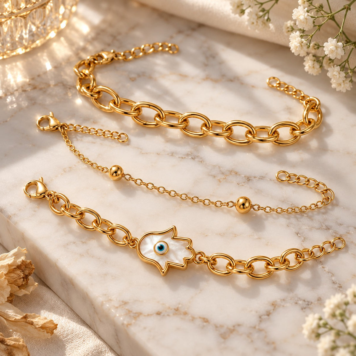 Gold hamsa evil eye bracelets styled on white marble with soft flowers
