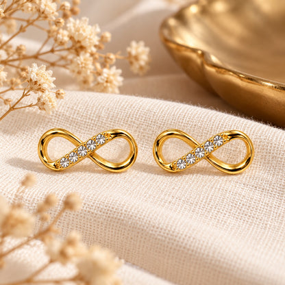 Gold infinity crystal stud earrings on cream linen with dried flowers