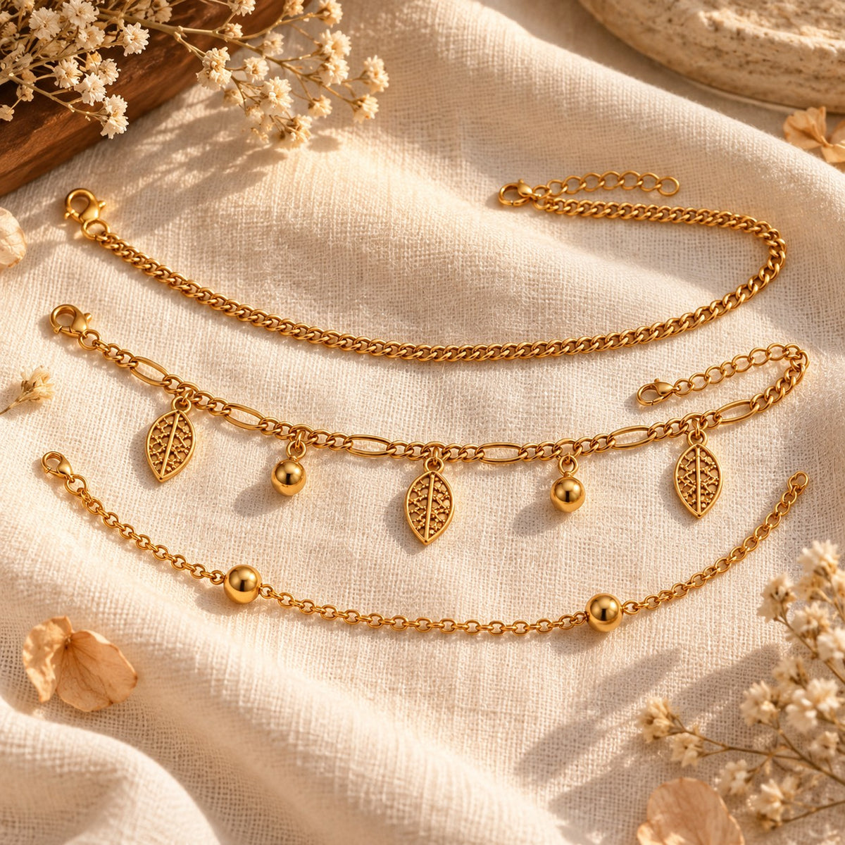 Gold leaf charm anklets styled on linen with dried flowers in warm light