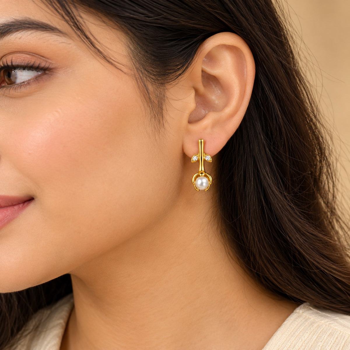 Woman wearing a gold rosebud pearl drop earring, close-up of ear and jawline
