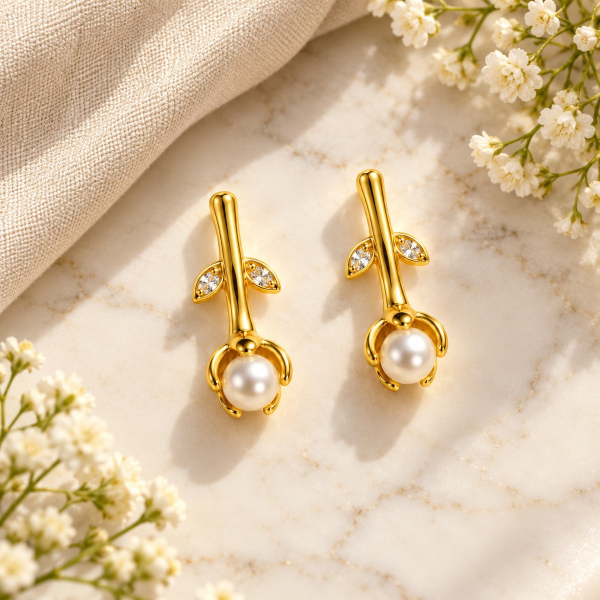 Gold rosebud pearl drop earrings on white marble with soft white flowers