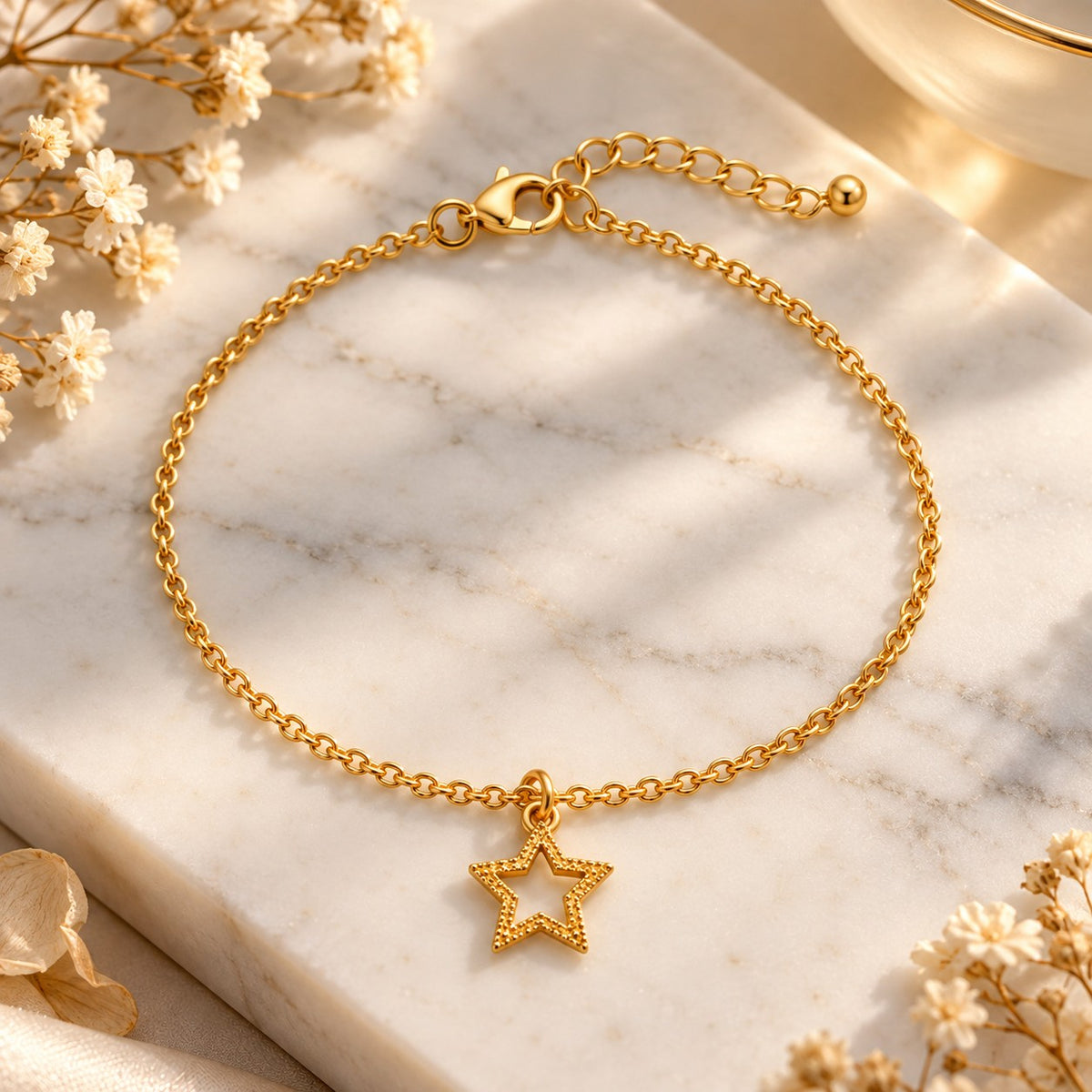 Gold star charm bracelet styled on white marble with soft flowers