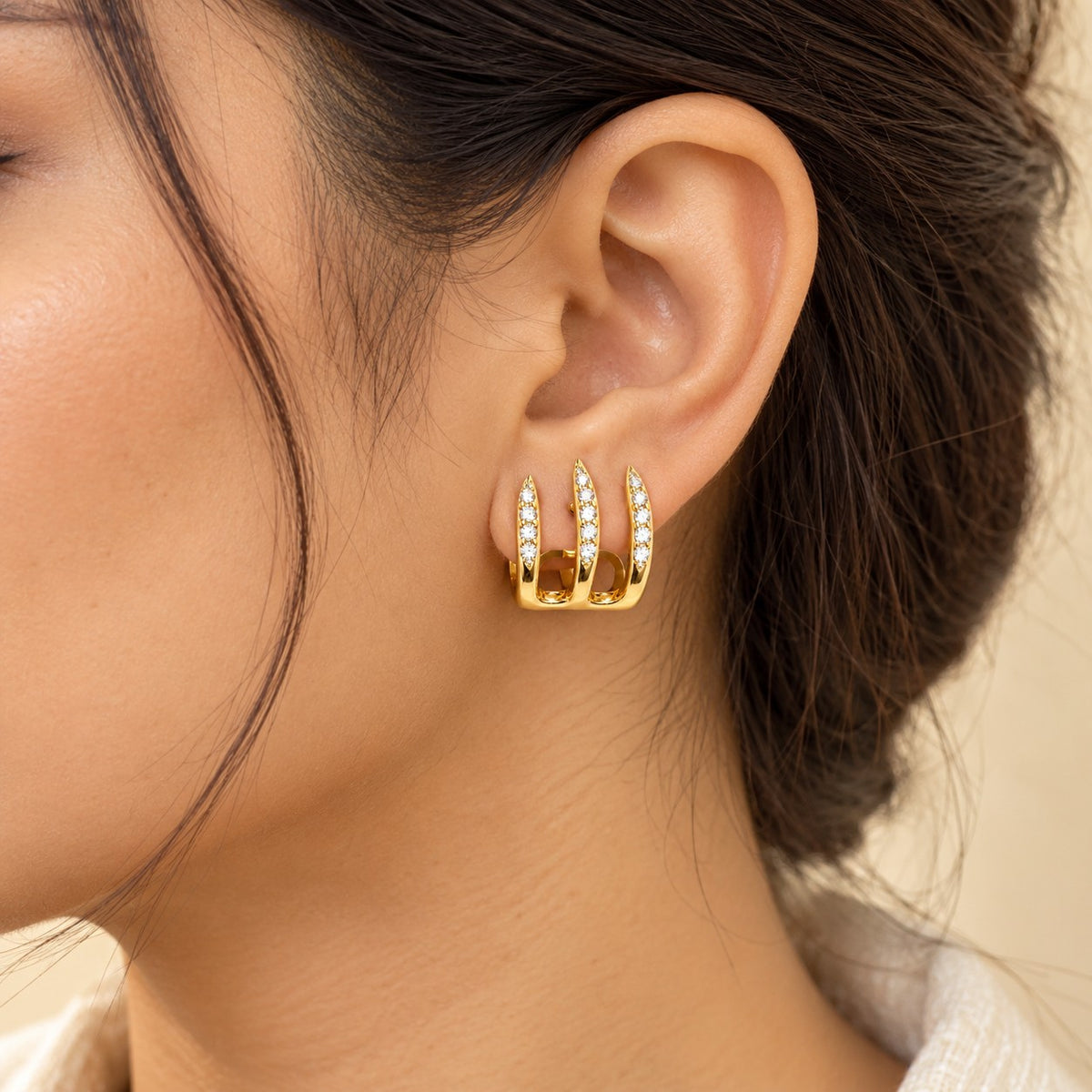 Woman wearing gold triple spike crystal hoop earrings, close-up of ear and jawline