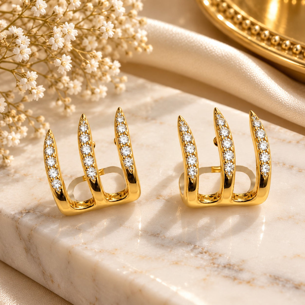 Gold triple spike crystal hoop earrings on a blush velvet jewellery box with petals