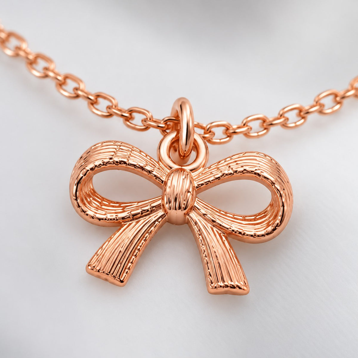 Close-up of the textured ribbon bow charm on the rose gold bow charm bracelet