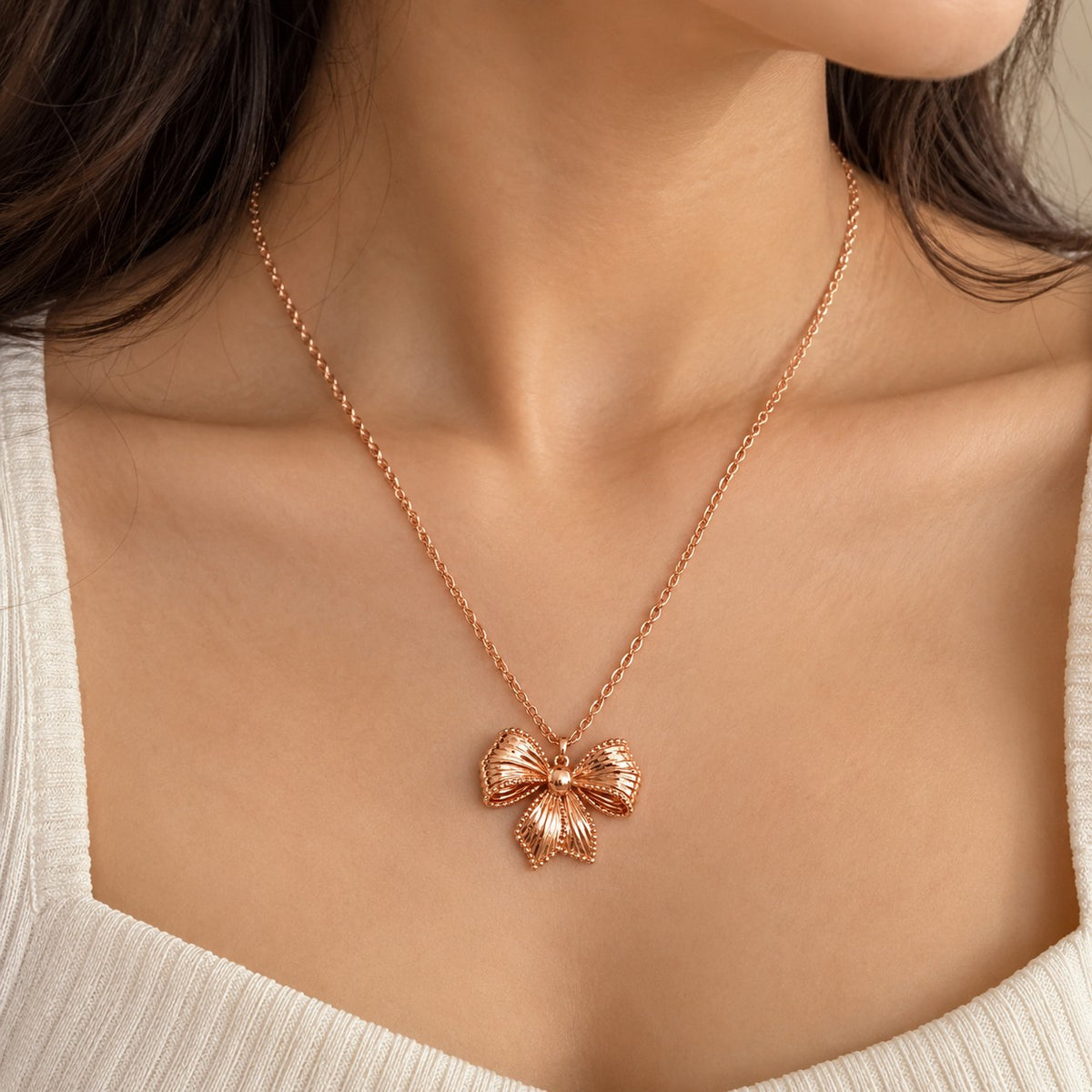 Woman wearing a rose gold bow pendant chain necklace at the neckline