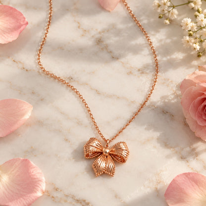 Rose gold bow pendant chain necklace on white marble with pink petals
