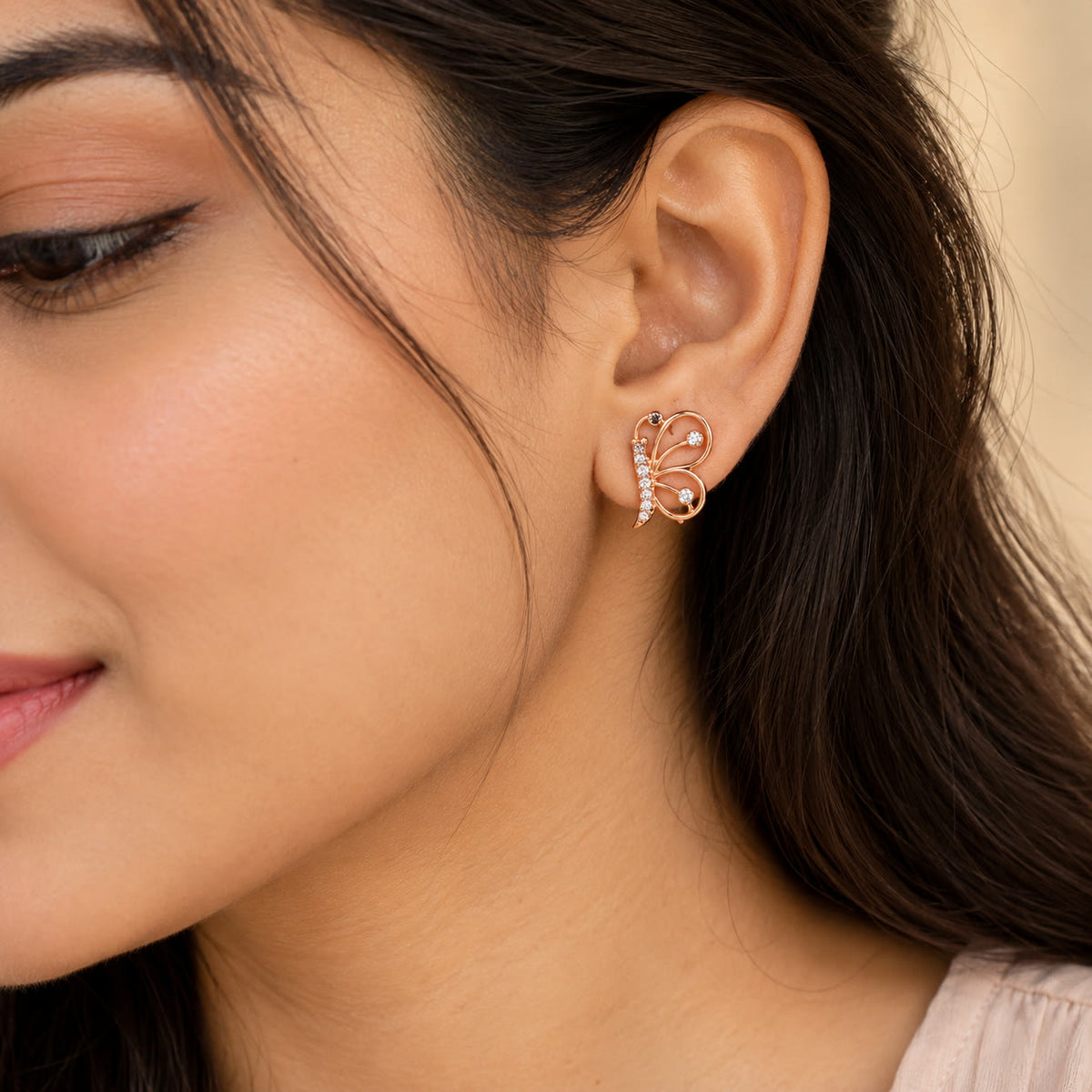 Woman wearing a rose gold butterfly stud earring with crystals, close-up of ear