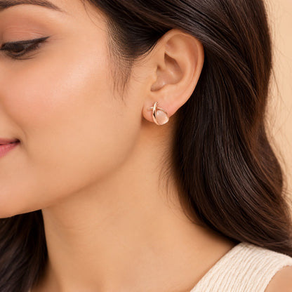 Woman wearing rose gold crossover peach stone stud earrings, close-up of ear and jawline