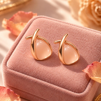Rose gold crossover peach stone stud earrings on a blush-pink velvet box with petals