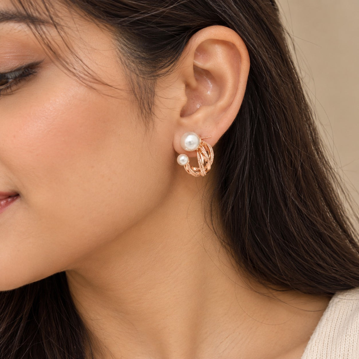 Woman wearing rose gold double pearl twisted hoop stud earrings, close-up of ear