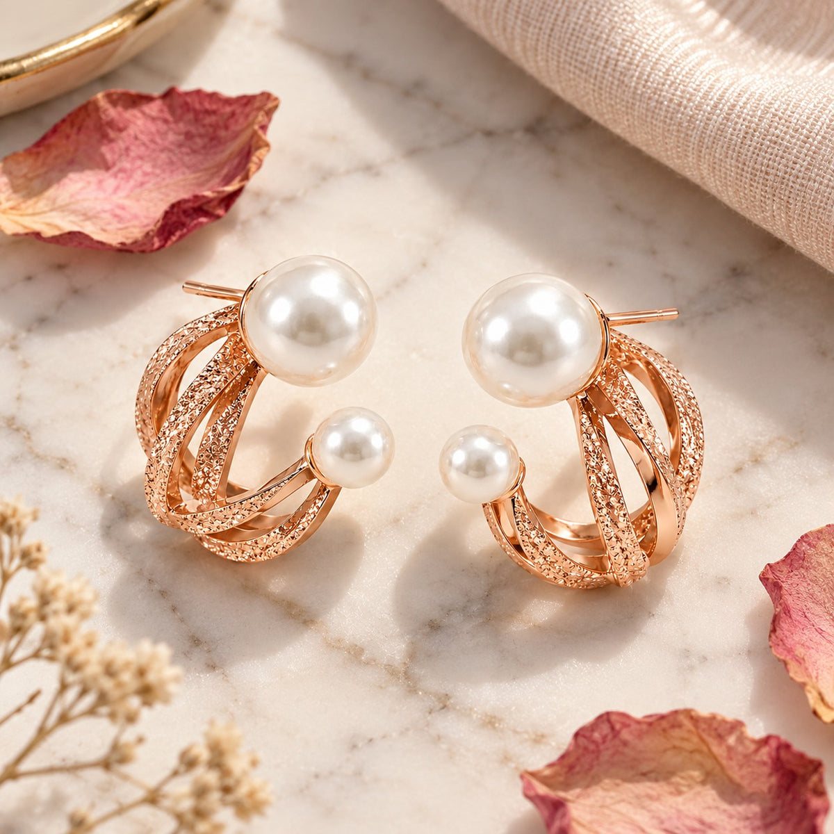 Rose gold double pearl twisted hoop stud earrings on white marble with dried petals