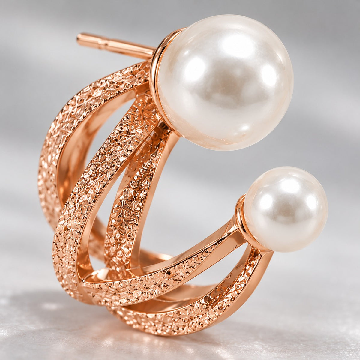 Macro of rose gold twisted bands and faux pearls on a double pearl hoop stud earring