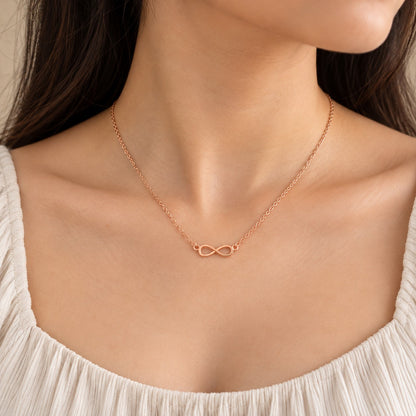 Woman wearing rose gold infinity pendant chain necklace, close-up of collarbone and neckline